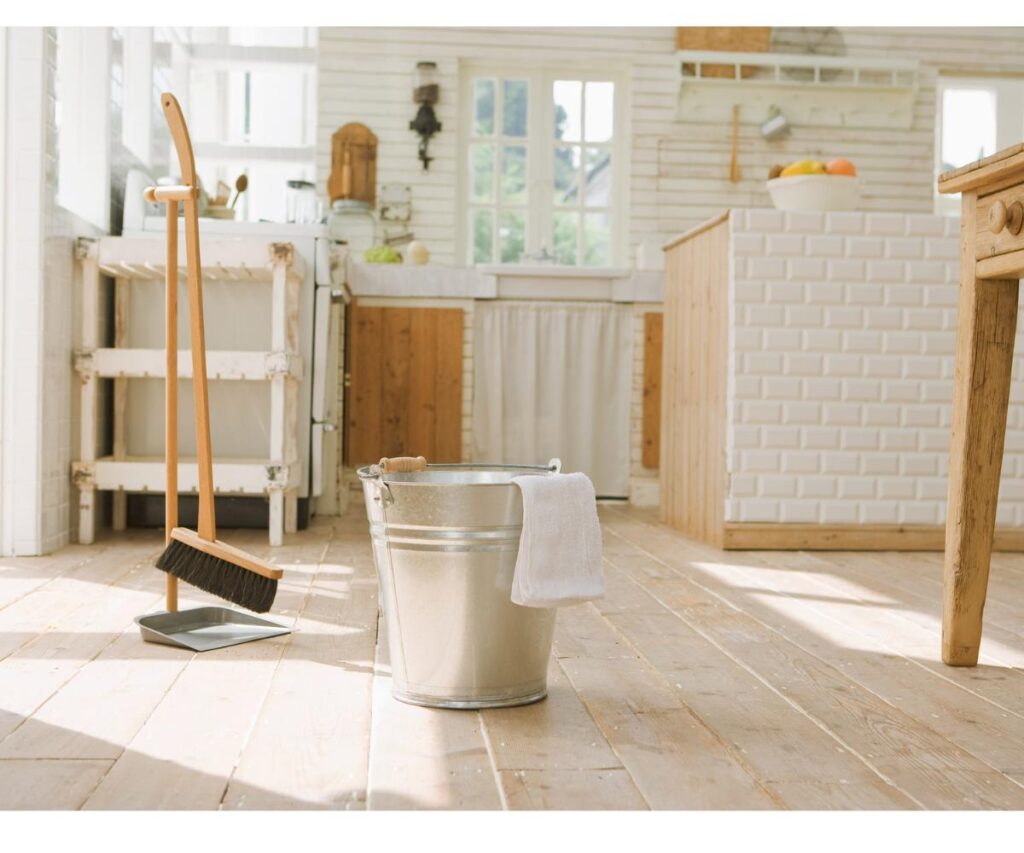 bucket with wash rag and broom in a sunny white kitchen.