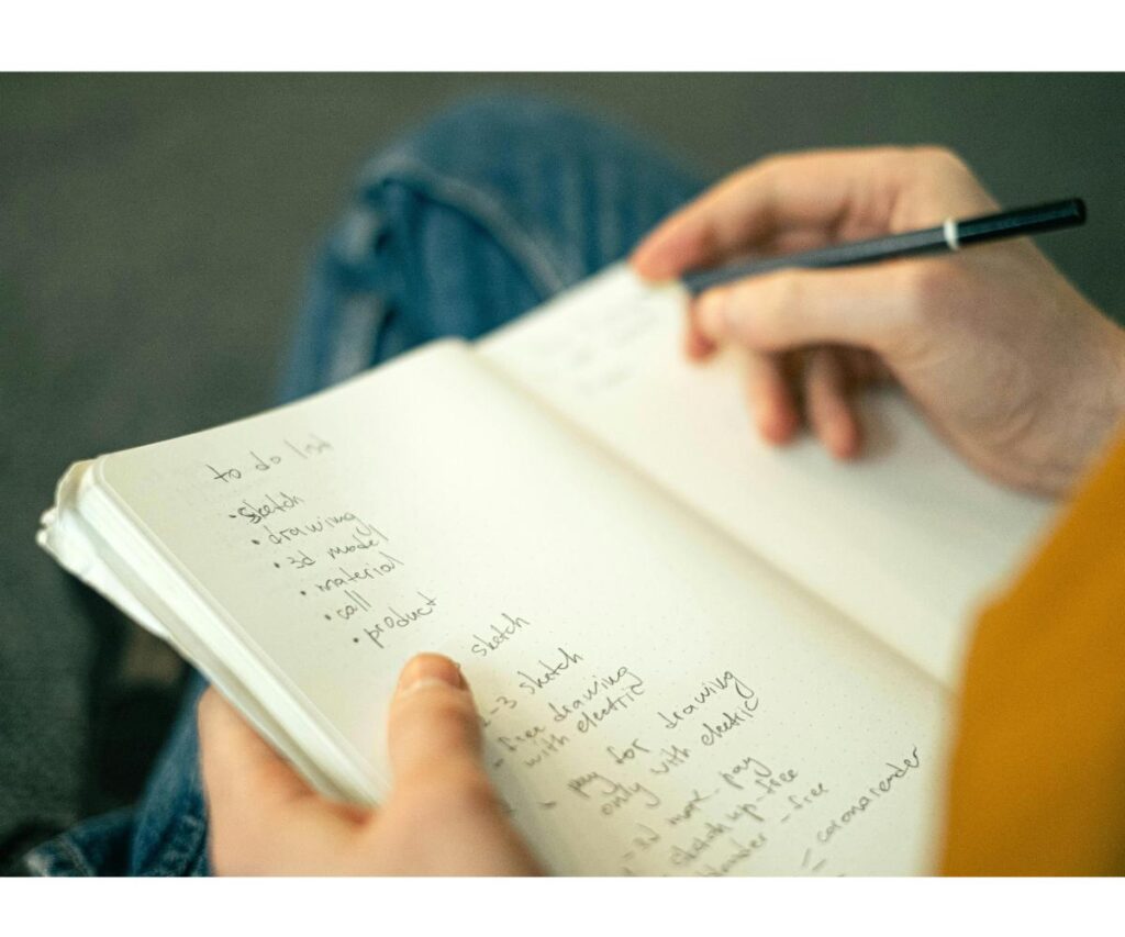 someone holding a notebook with a to do list written inside, and holding a pen.