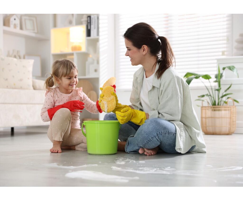 a mom and daughter with a cleaning bucket and sponge on the floor.